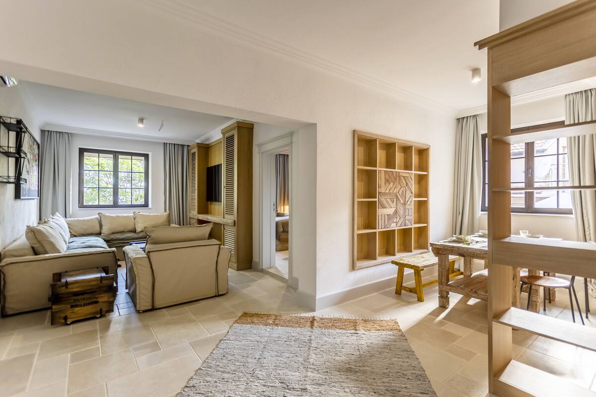 A spacious living room with a sofa set, wooden shelves, and a dining area.