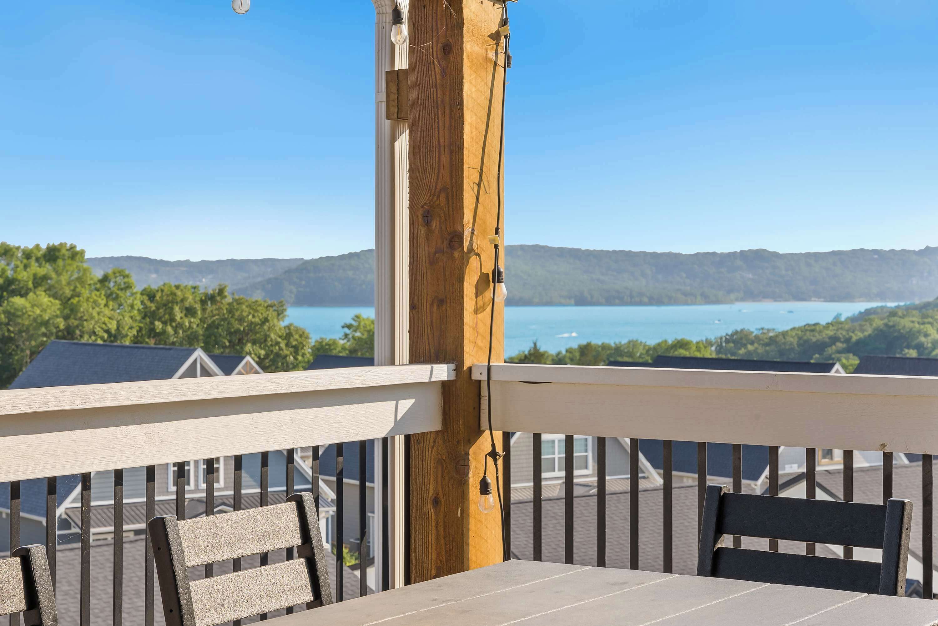 Un balcon doté d’une balustrade en bois, d’une table et de deux chaises. Un luminaire est suspendu à la balustrade. La vue comprend un lac et des collines lointaines.