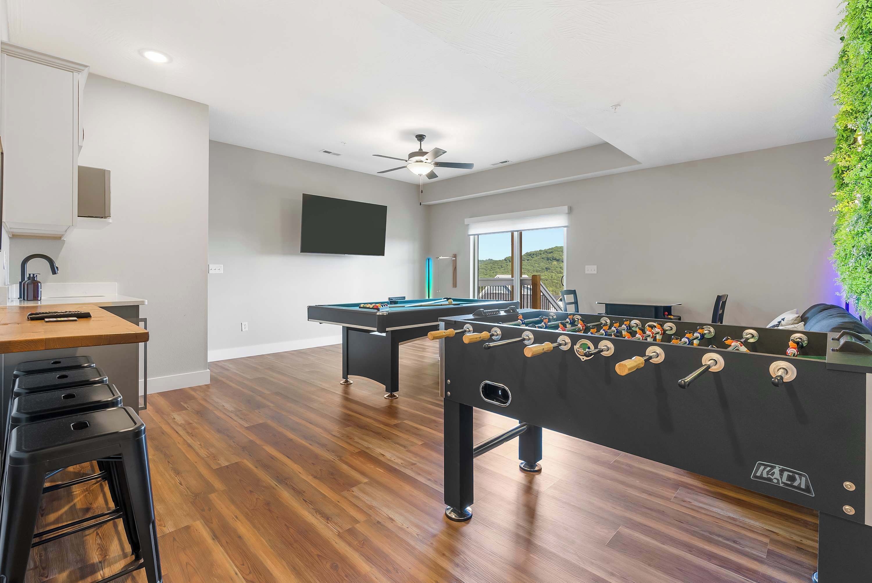 A spacious room with a foosball table, a pool table, and a bar area with stools.