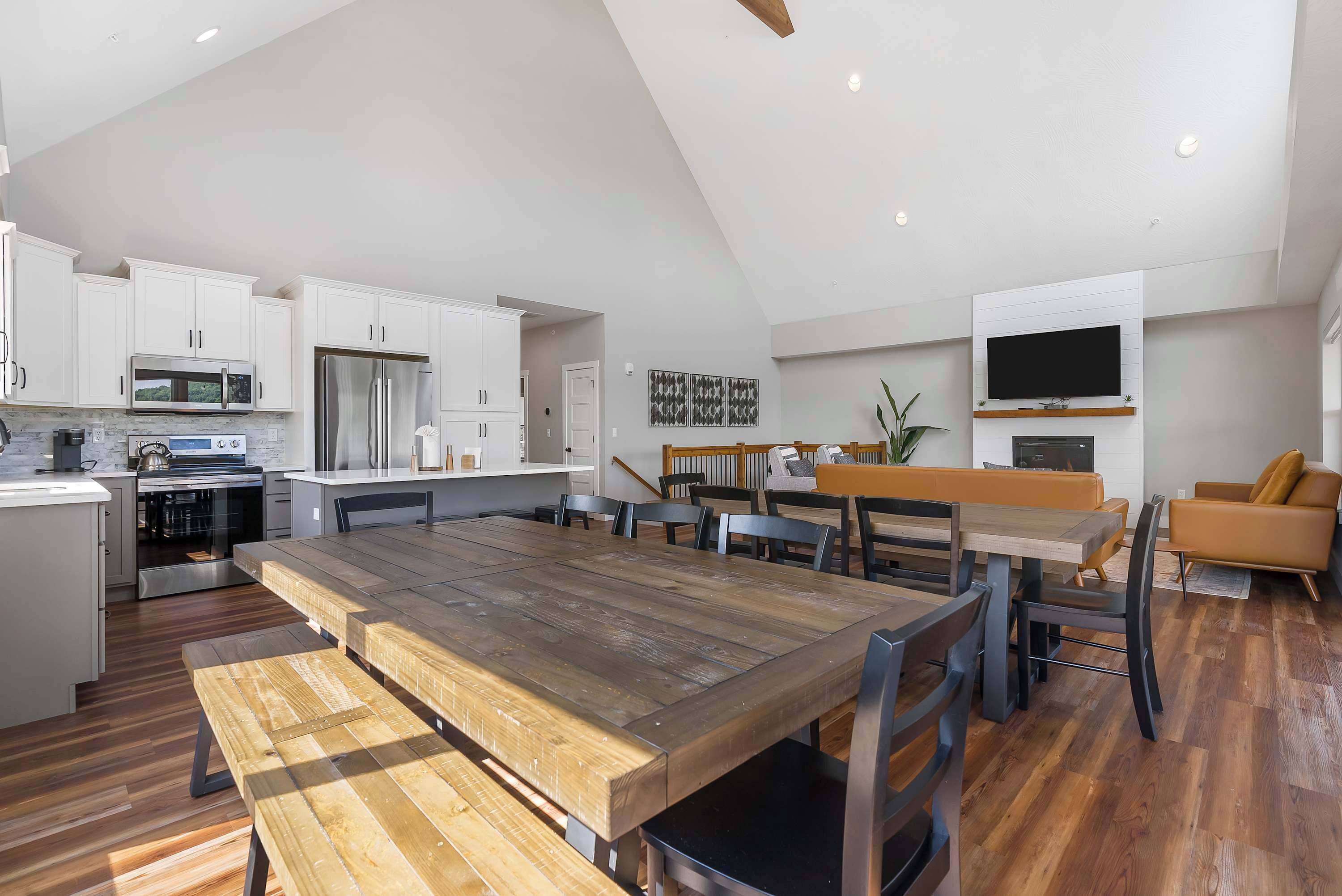 Une cuisine spacieuse avec des meubles blancs, une table à manger en bois et un téléviseur moderne.