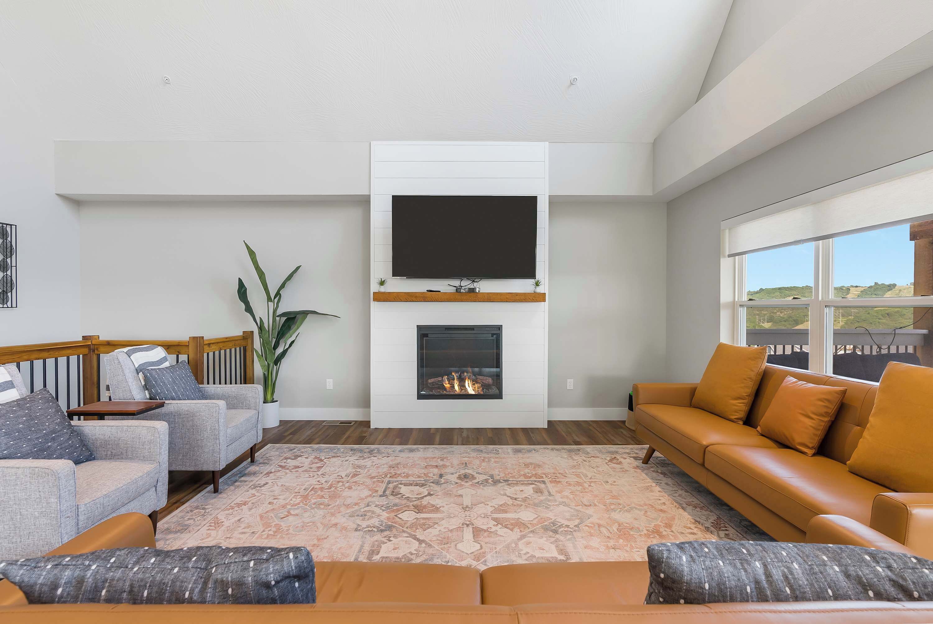 A modern living room with a fireplace, a large TV mounted on the wall, and a sofa set.