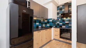 A modern kitchen with a black refrigerator, wooden cabinets, a tiled backsplash, and a built-in oven. - Stylish Apartment in Krakow | Balcony and Workspace (Kraków)