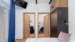 A bedroom with a bed, a wooden wardrobe, a TV mounted on the wall, and a view into the adjacent room through a door. - Stylish Apartment in Krakow | Balcony and Workspace (Kraków)