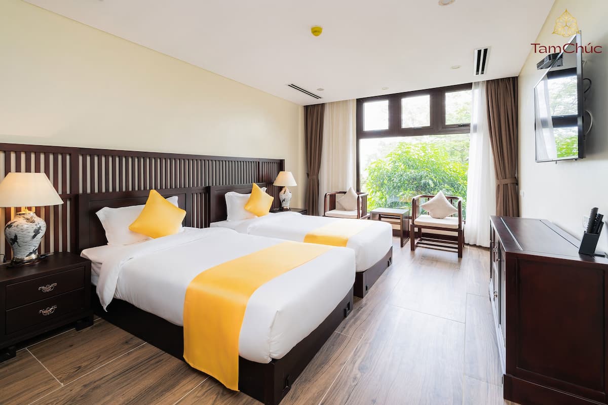 Une chambre d’hôtel avec deux lits, une télévision, un bureau et une vue sur la verdure environnante.