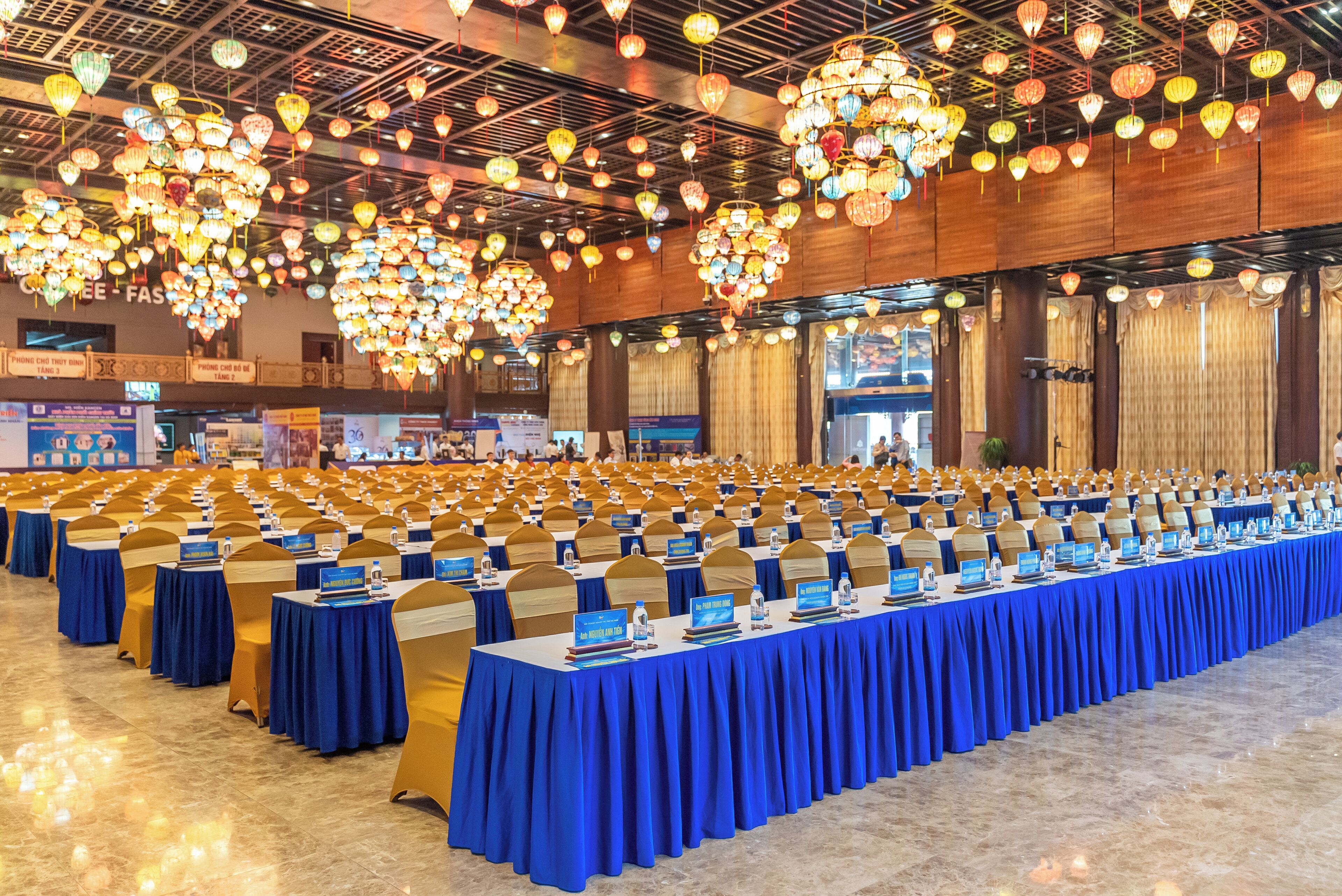 A conference room with rows of tables, blue tablecloths, and gold chairs.