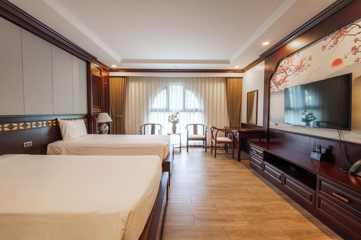 Une chambre d’hôtel avec deux lits, un bureau, des chaises, une télévision et une grande fenêtre avec des rideaux.
