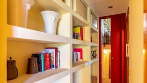 A hallway with a red door, white shelves with books and decorative items, and a tiled floor. - GuestHost - Naxos Seaside Apt with Gardens, Parking and Pool (Giardini Naxos)