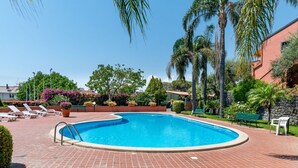 A swimming pool with a brick deck, surrounded by palm trees and lounge chairs. - GuestHost - Naxos Seaside Apt with Gardens, Parking and Pool (Giardini Naxos)