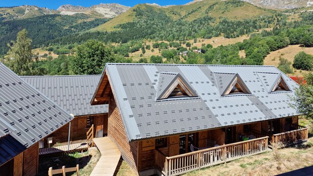 A lodge with a metal roof and wooden exterior, set against a mountainous backdrop.