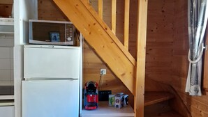 A wooden staircase leading to a lower level, a white refrigerator, a coffee maker, and a trash bin in a cabin-style kitchen.