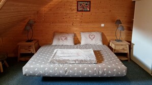 A cozy bedroom with a sloped ceiling, wooden walls, a bed with a heart-patterned pillow, two bedside lamps, and a framed picture on the wall.