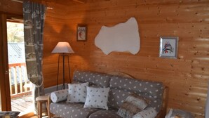 A cozy cabin interior with a wooden wall, a sofa with patterned cushions, a floor lamp, and a framed picture on the wall.