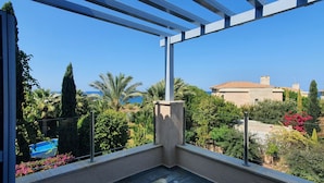 A balcony with a view of a coastal area, including a building with a tiled roof and palm trees. - Phaedrus Living: Amorosa 13 Beachside Villa (Neo Chorio)