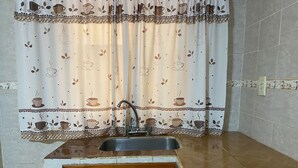 A kitchen with a sink, wooden cabinets, and a patterned curtain. - Hotel Itavera (Puerto Iguazú)