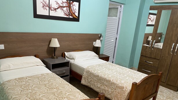 A hotel room with two wooden beds, a nightstand with a lamp, a wardrobe, and a wall-mounted artwork. - Hotel Itavera (Puerto Iguazú)