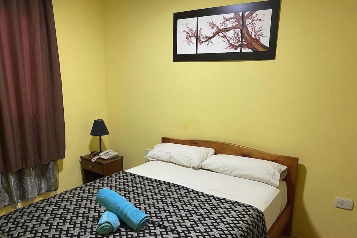 Ein Hotelzimmer mit einem Bett, einem Nachttisch, einer Lampe, einem Telefon und einem Wandbild.