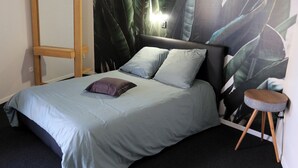 Une chambre à coucher avec un lit, une table de chevet, un miroir et une grande fresque murale représentant des plantes tropicales.