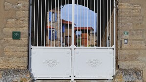 Un bâtiment en pierre avec un portail blanc orné de barreaux en métal décoratifs et d’un motif floral.