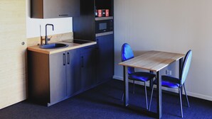 Une cuisine moderne avec un plan de travail en bois, des armoires noires et un four encastré. On y trouve une table à manger avec des chaises bleues et un luminaire suspendu.
