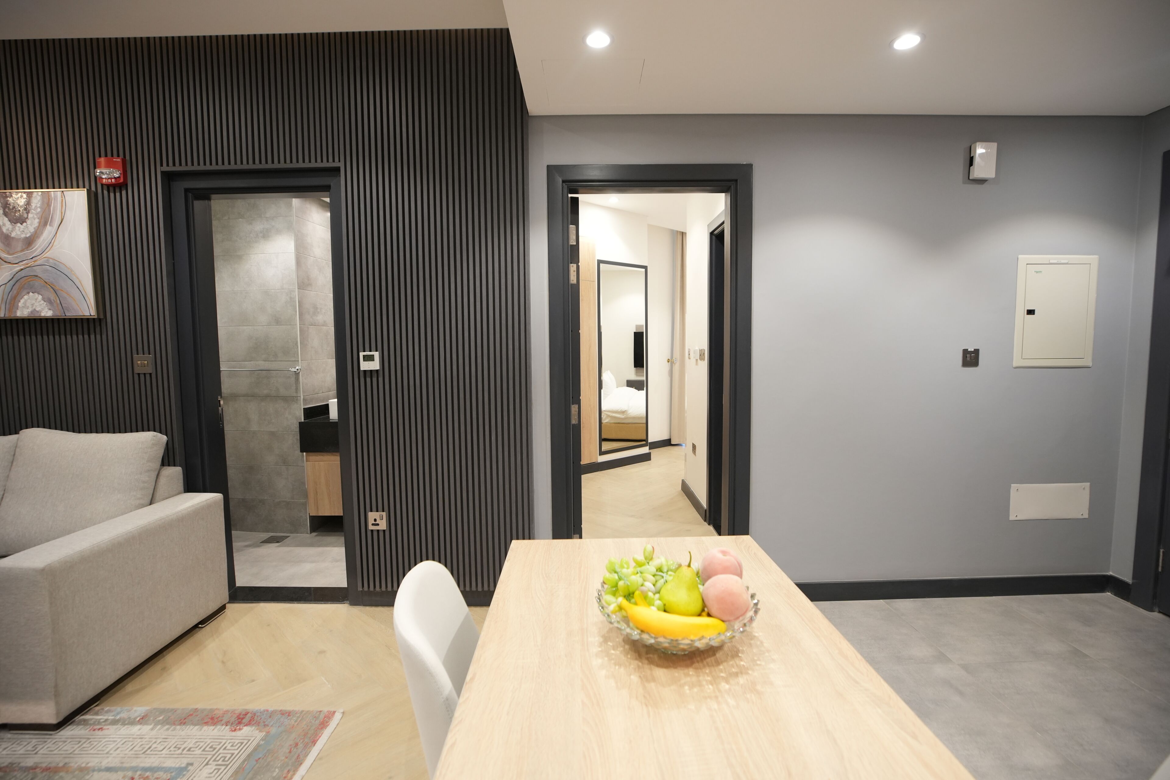 Een moderne woonkamer met een bank, een eettafel met een schaal fruit en uitzicht op de keuken.