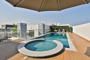 Una piscina en la azotea con un jacuzzi, sillas de descanso y una barandilla de cristal.