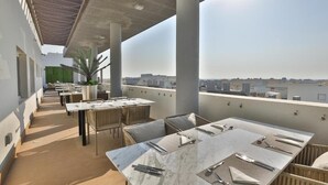 An outdoor dining area with marble tables and wicker chairs, overlooking a cityscape. - Royal Mansoura Residence Hotel (Doha)