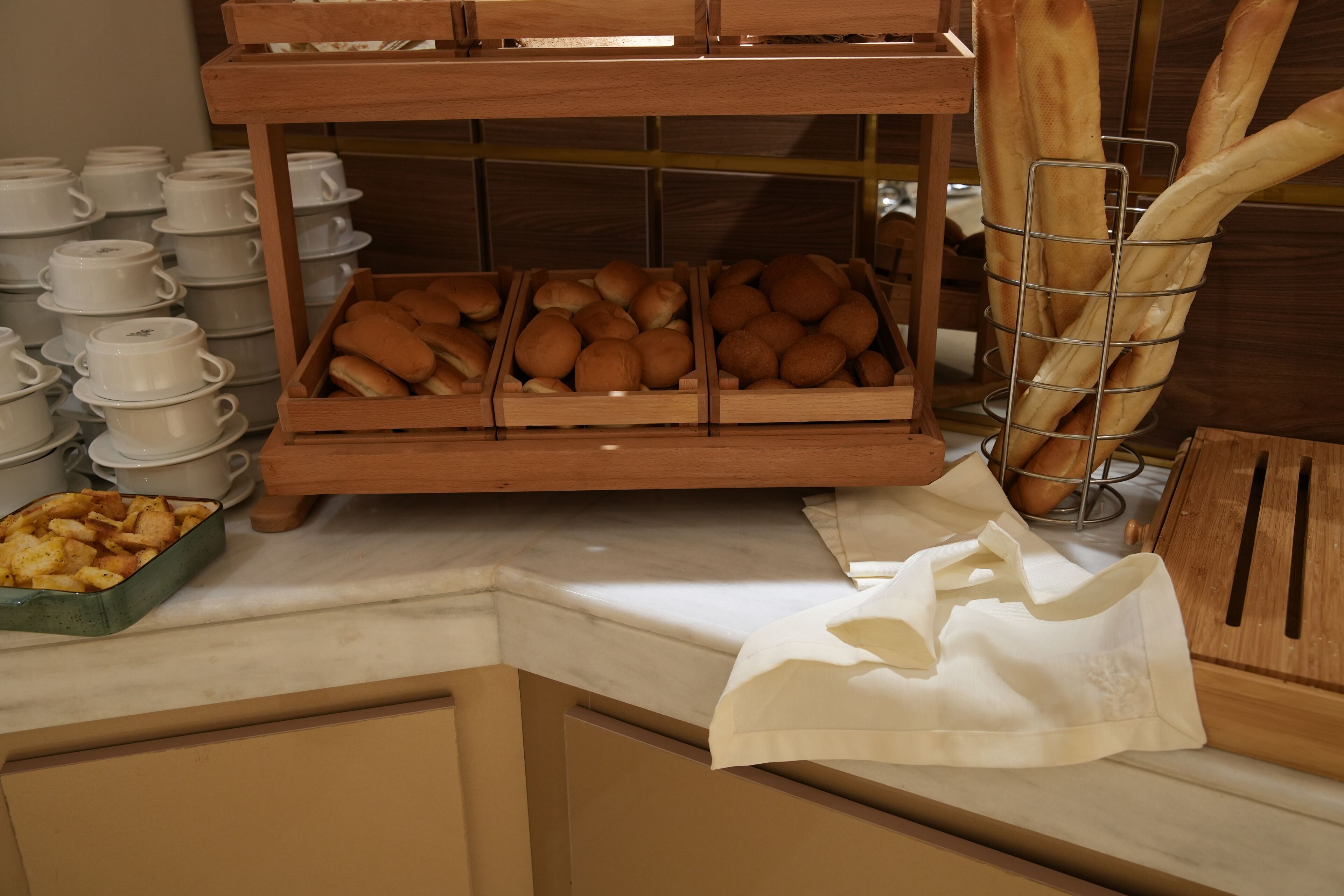 A buffet setup with bread, pastries, and white cups.