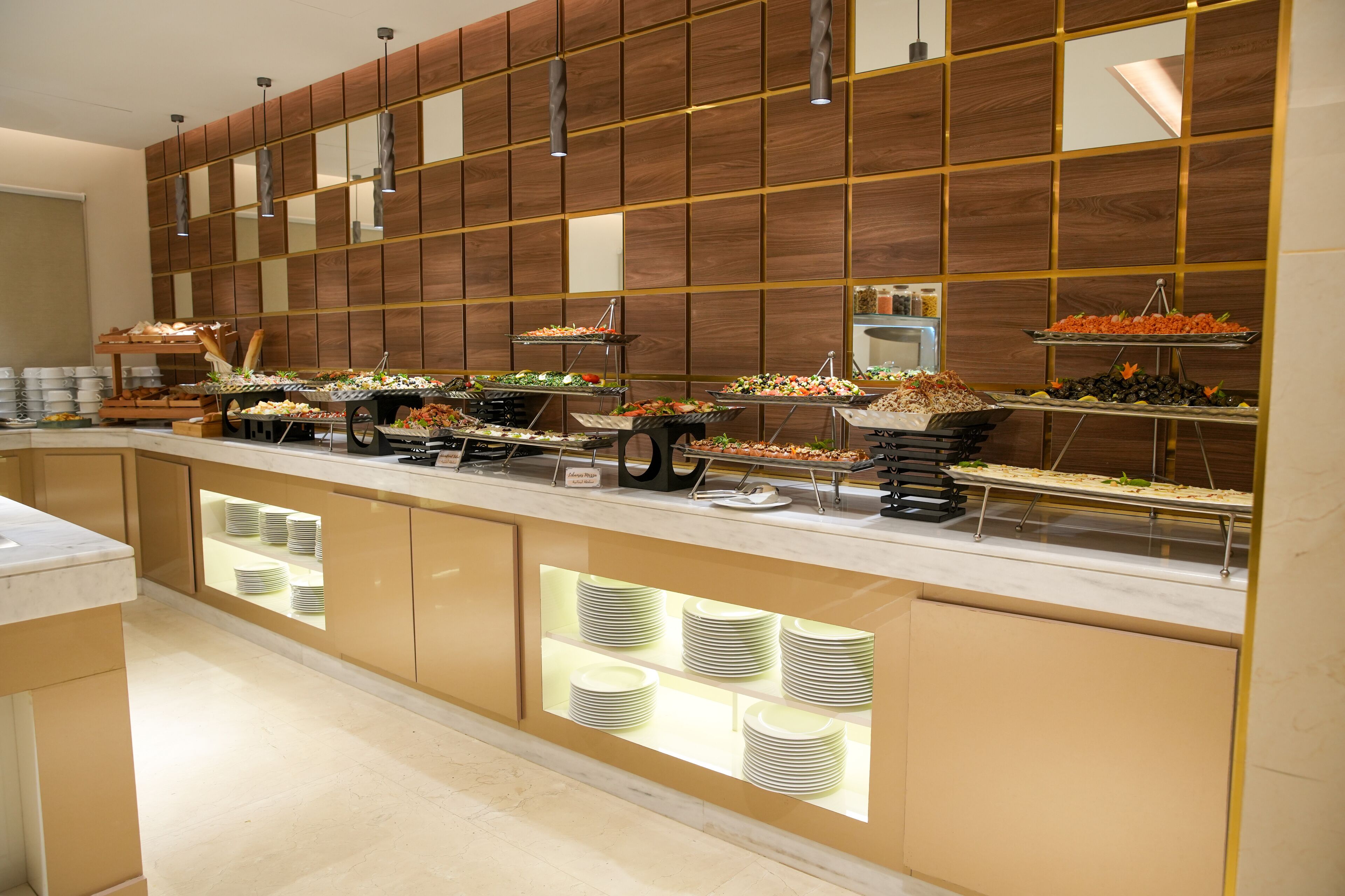 Un'area buffet con diverse postazioni gastronomiche e un banco con piatti impilati.