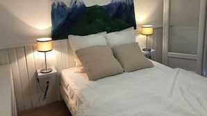 A neatly made bed with two pillows, a wall-mounted painting of mountains, and two bedside lamps.