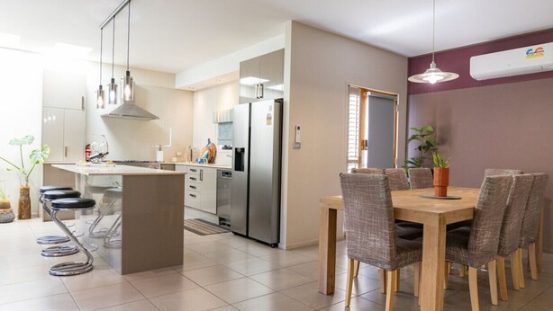 A modern kitchen with a central island, dining table with chairs, and a refrigerator.