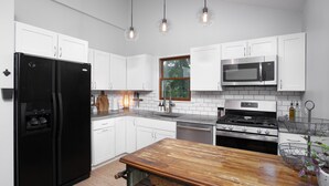 Eine moderne Küche mit weißen Schränken, einem schwarzen Kühlschrank, Edelstahlgeräten und einem Holztisch.