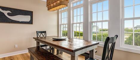 A dining area with a wooden table and benches, large windows, and a hanging light fixture.