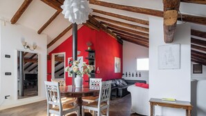 A modern living room with a dining area, red walls, wooden beams, and a white sofa.