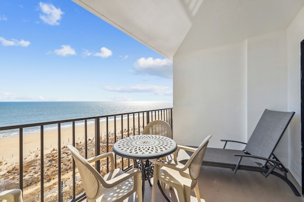 A balcony with a table and chairs, overlooking a beach.