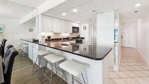 A modern kitchen with white cabinets, a black countertop, and a large island with bar stools. - XPLORIE ACTIVITIES & LINENS INCLUDED*! Direct Oceanfront 2 bedroom (enclosed den converted to a 3rd bedroom with new double bed & pocket door) 2 bath condo. (Ocean City)