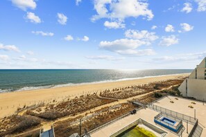 Vista de una playa con cielo despejado, arena y un edificio con piscina.