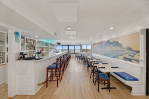 A restaurant with a bar, wooden tables, and chairs, and a large window with a cityscape view.