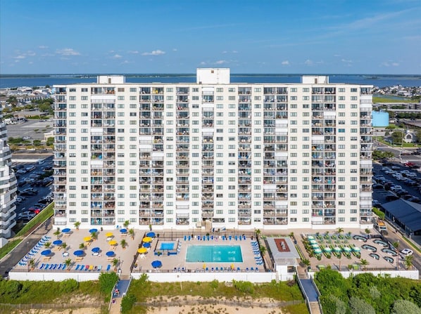 A high-rise hotel with multiple balconies, a swimming pool, and a parking area.