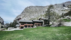 Un albergue de montaña con fachada de piedra, balcones de madera y vistas a una montaña nevada.