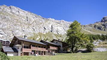 A mountain lodge with multiple balconies and a stone facade, set against a backdrop of rocky mountains and a clear sky.