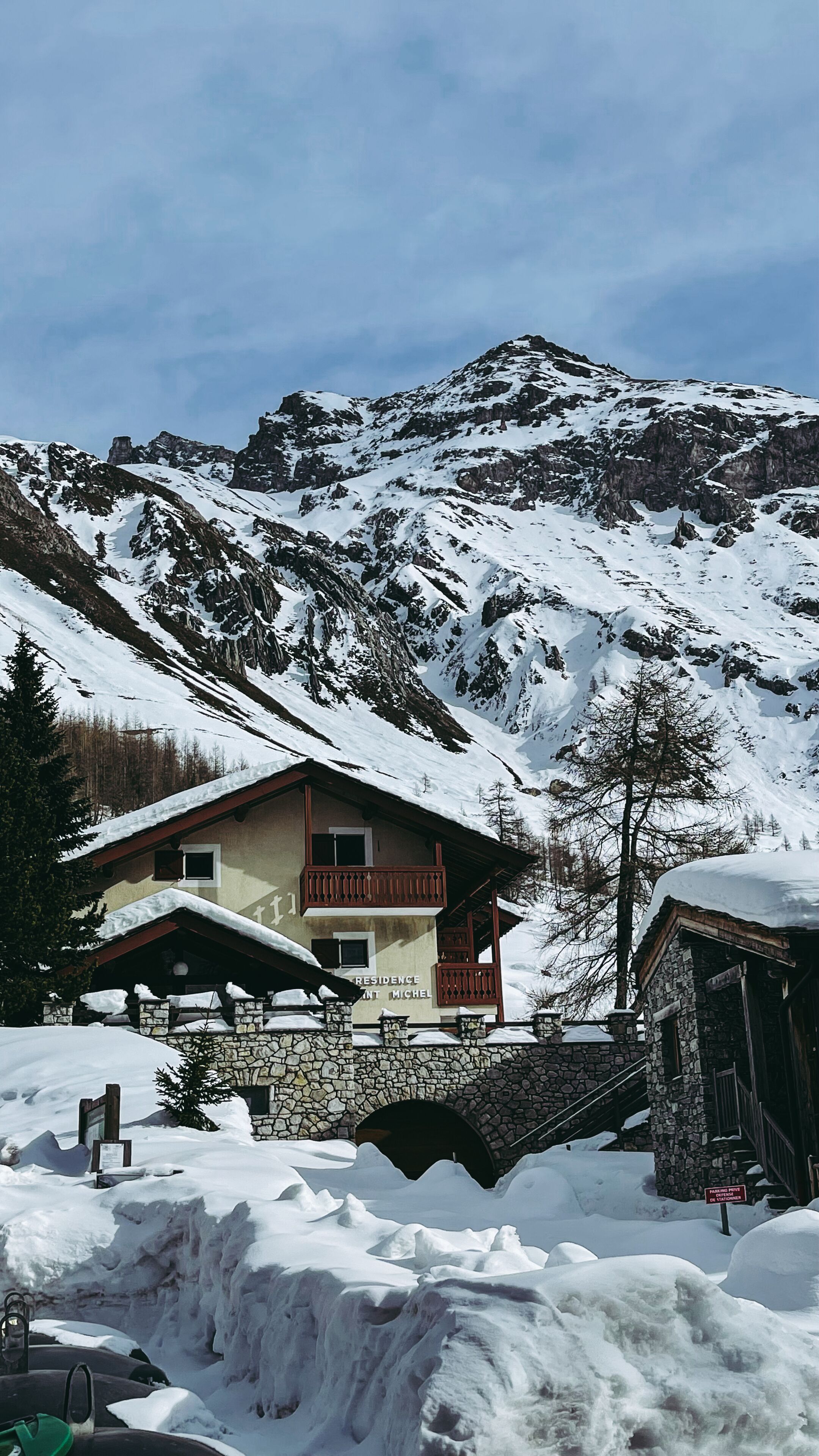 A mountain lodge with a stone facade, wooden balconies, and a sign indicating 'Residence Michel'.