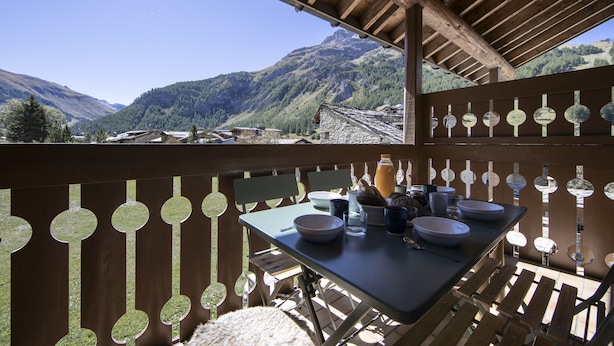 Terraza de madera con mesa lista para comer, con vistas a un paisaje montañoso.
