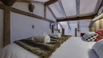 Een slaapkamer met een groot bed, houten balken, een bontje en een opgehangen dierenhoofd.