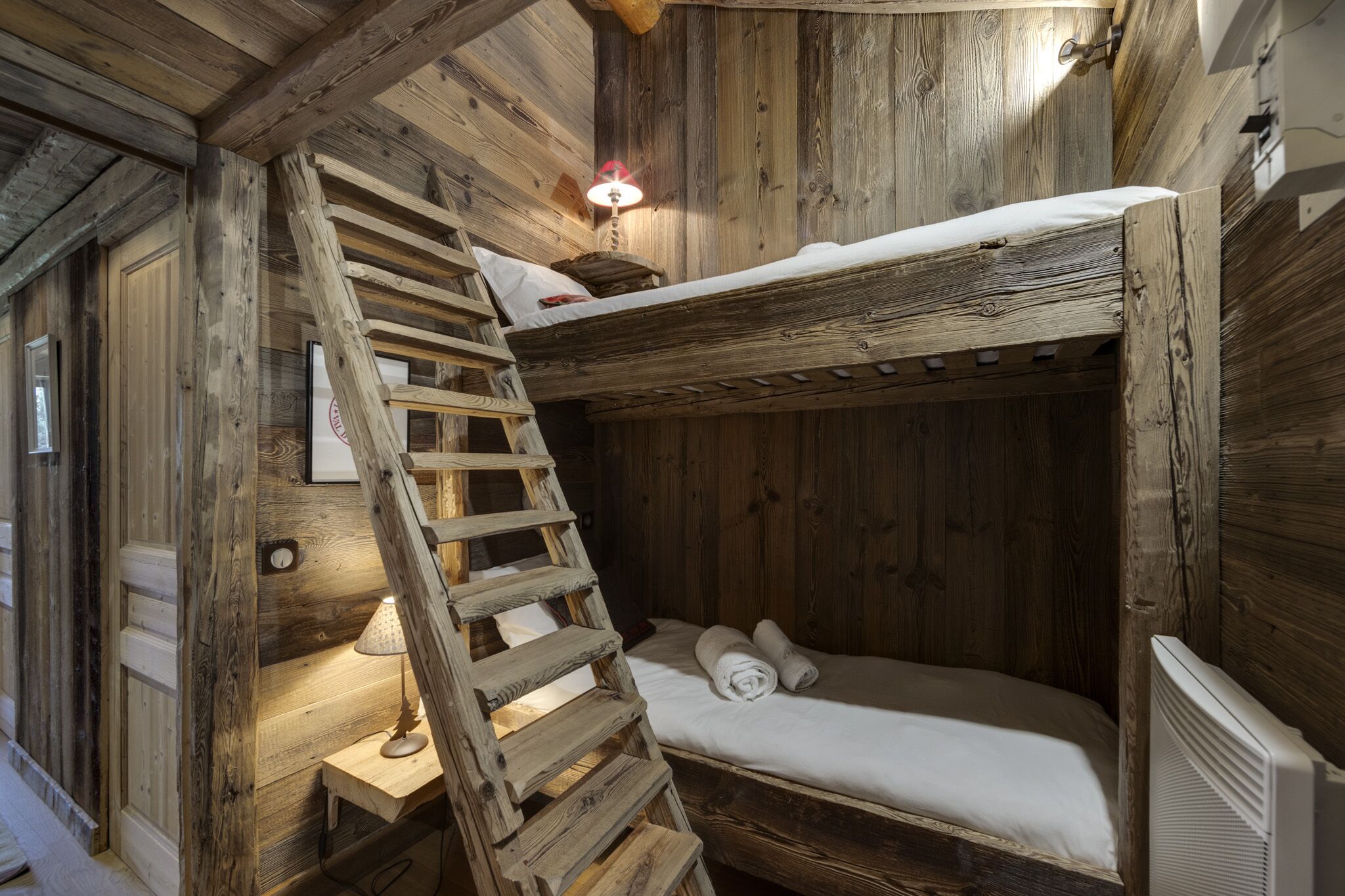 Une pièce rustique en bois, avec un lit superposé, une échelle en bois, une petite table avec une lampe et un radiateur.