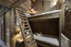 Une pièce rustique en bois, avec un lit superposé, une échelle en bois, une petite table avec une lampe et un radiateur.