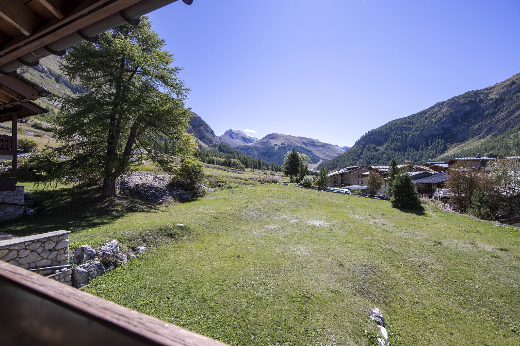 Un borgo montano con case tradizionali, un cortile erboso e una vista chiara delle montagne circostanti.