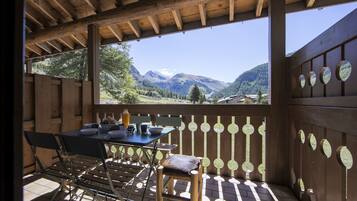 Eine Holzdielen-Terrasse mit Tisch und Stühlen, mit Blick auf eine gebirgige Landschaft.