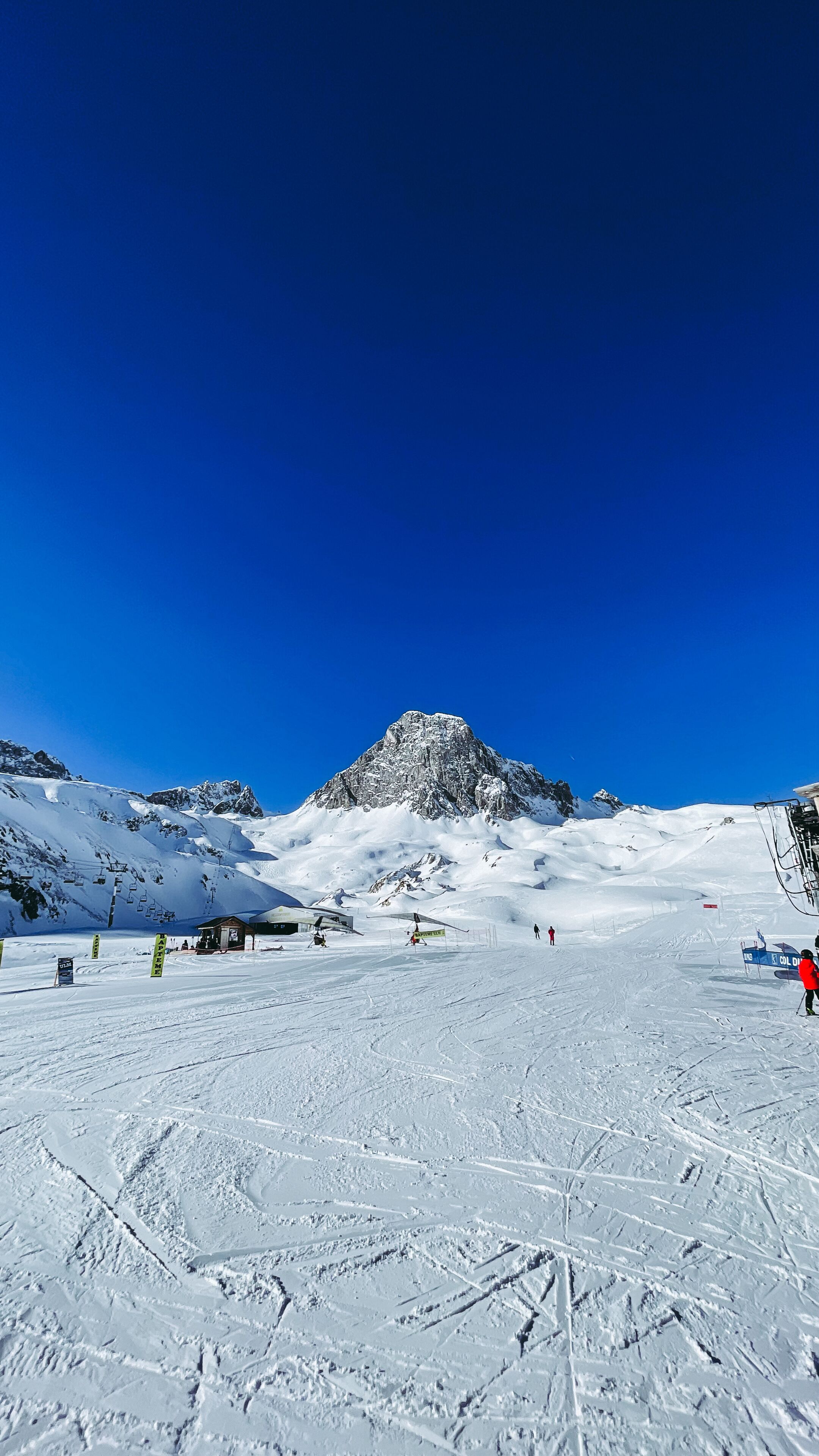 Une piste de ski enneigée, avec une montagne en arrière-plan, des remontées mécaniques et quelques skieurs.