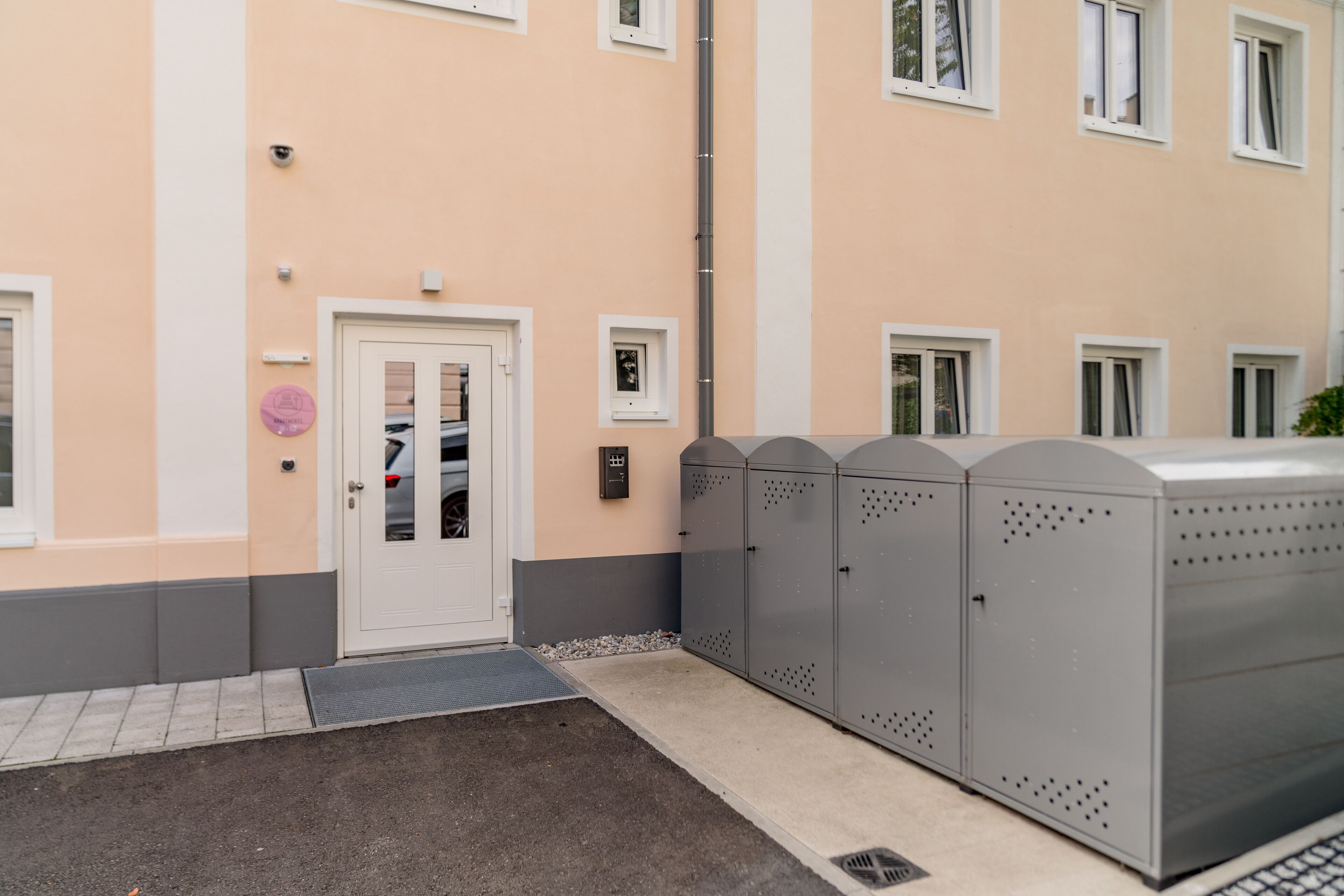 A building with a white door, a security camera, and a metal storage unit.