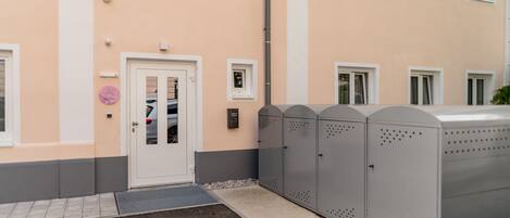 A building with a white door, a security camera, and a metal storage unit.